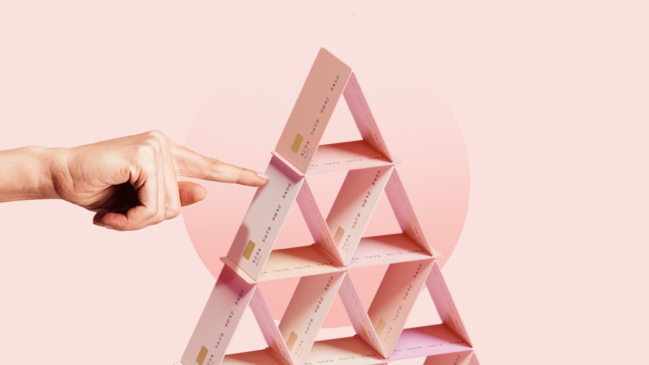 Hand pokes pyramid of stacked credit cards in front of a pink background