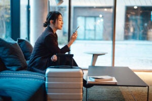 Business woman doing online check-in with smartphone while sitting at hotel lobby, getting ready to depart. Young woman on business trip.
