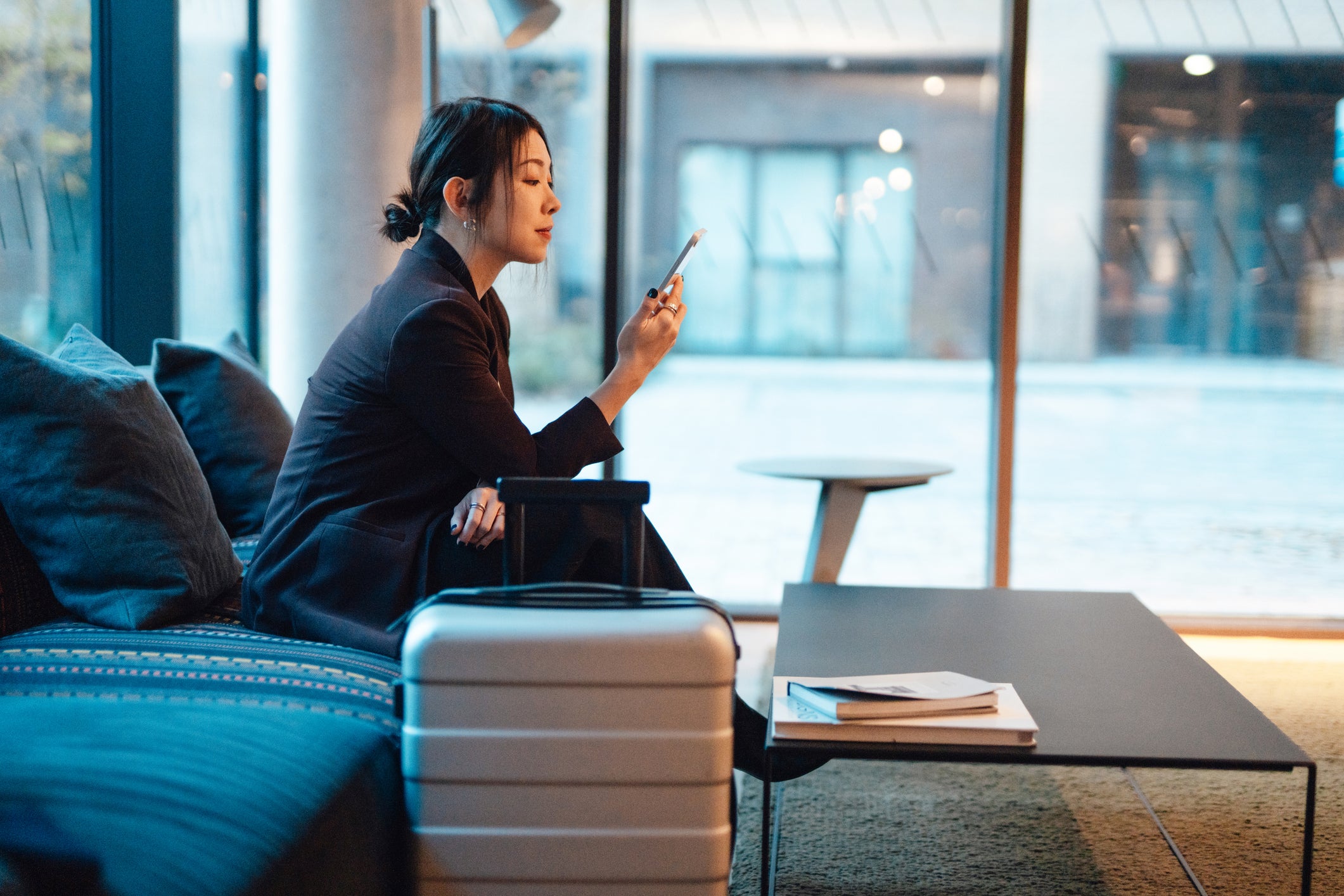 Business woman doing online check-in with smartphone while sitting at hotel lobby, getting ready to depart. Young woman on business trip.