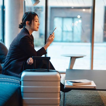 Business woman doing online check-in with smartphone while sitting at hotel lobby, getting ready to depart. Young woman on business trip.