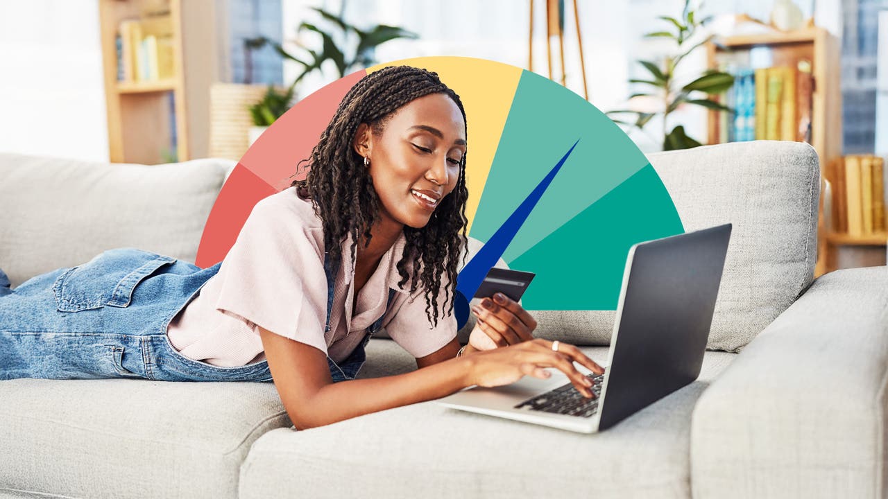Woman lying down on a couch looking at a credit card and laptop