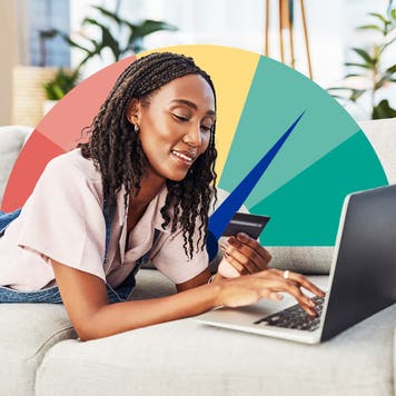 Woman lying down on a couch looking at a credit card and laptop
