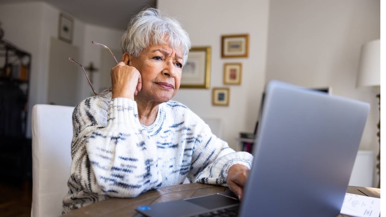 A concerned senior woman reads about annuities on her laptop.