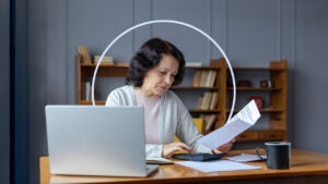 Older woman sitting at her kitchen table with a laptop and looking at her policy