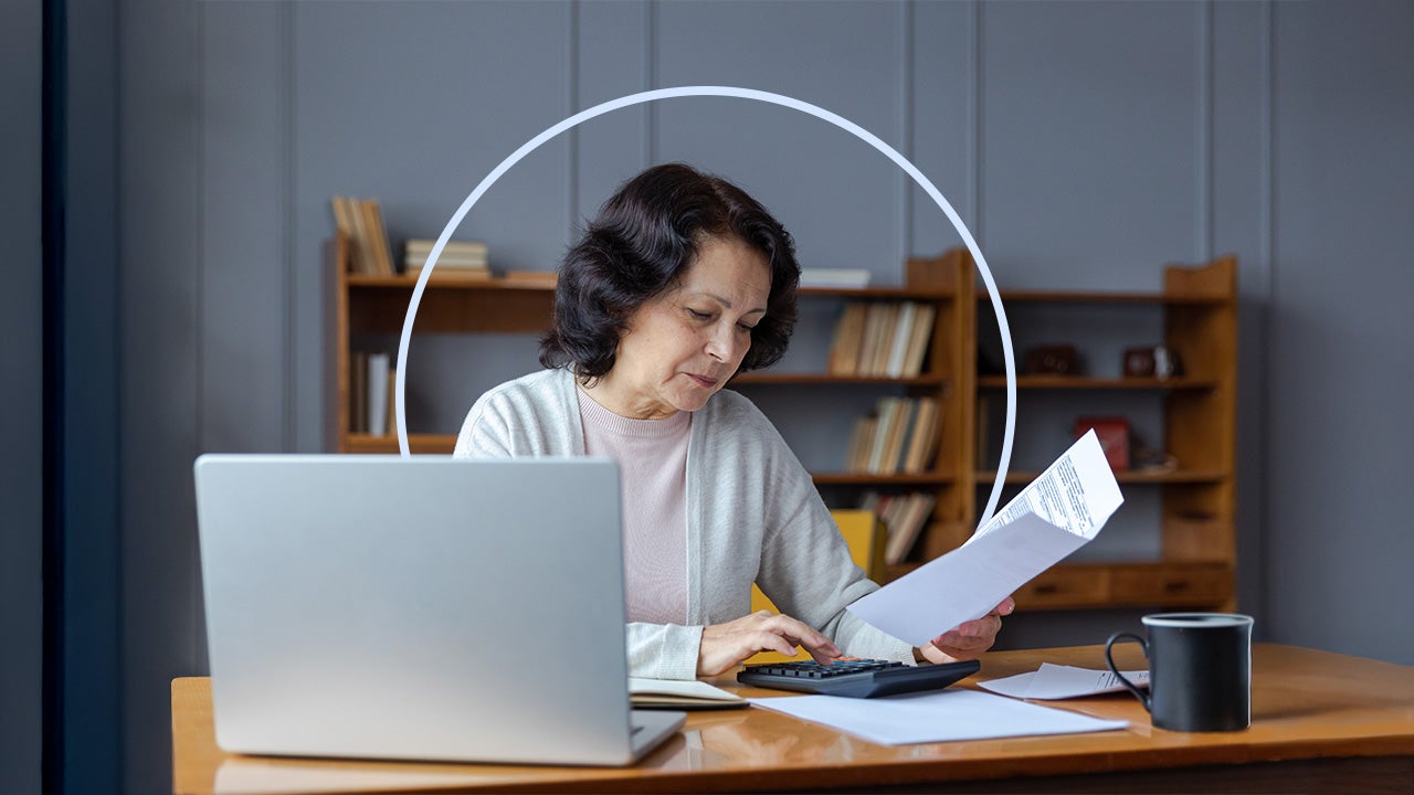 Older woman sitting at her kitchen table with a laptop and looking at her policy