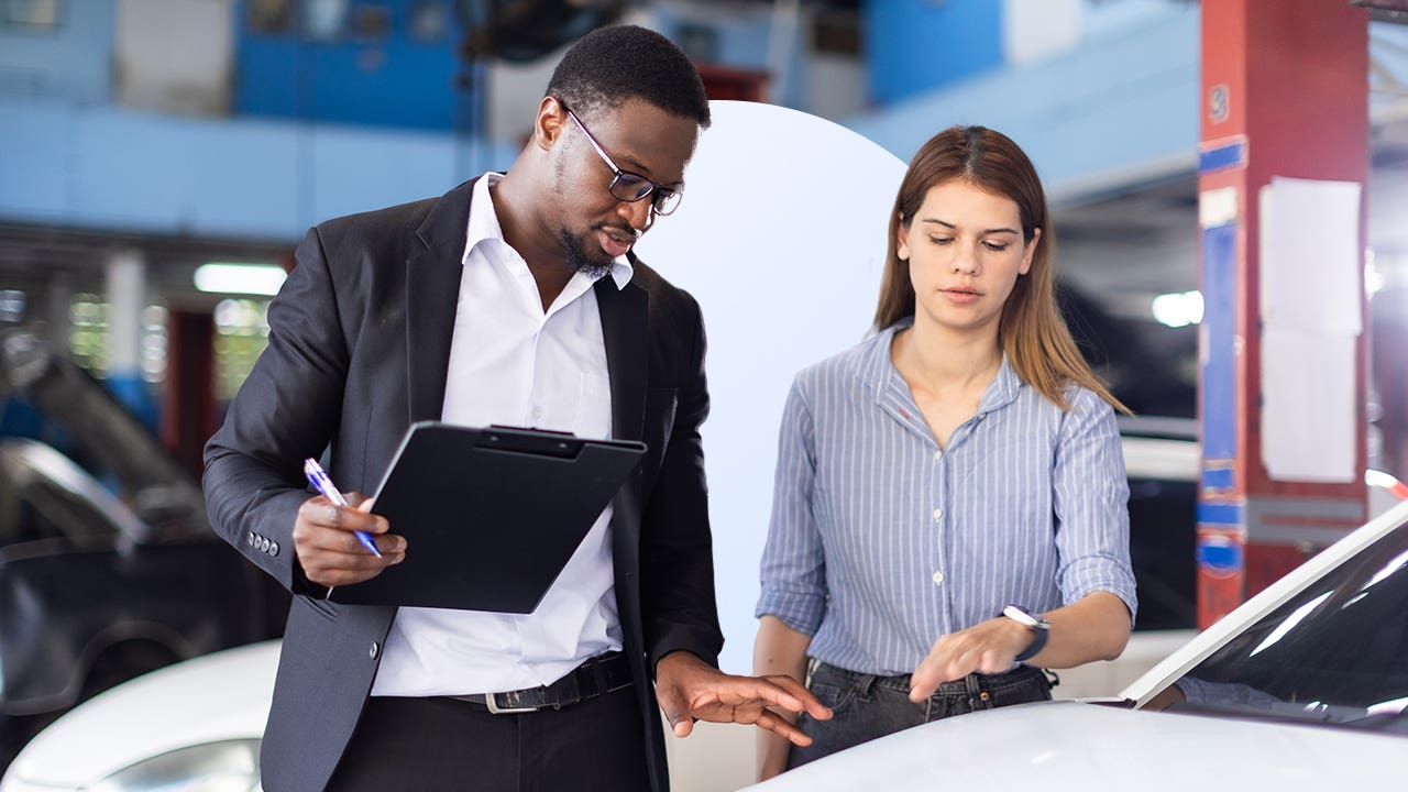 man and woman in car repair shop standing near car discussing its condition