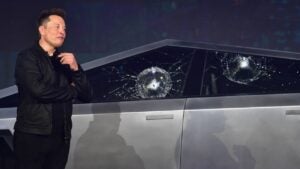 Tesla CEO Elon Musk standing next to a Cybertruck with damaged side windows.