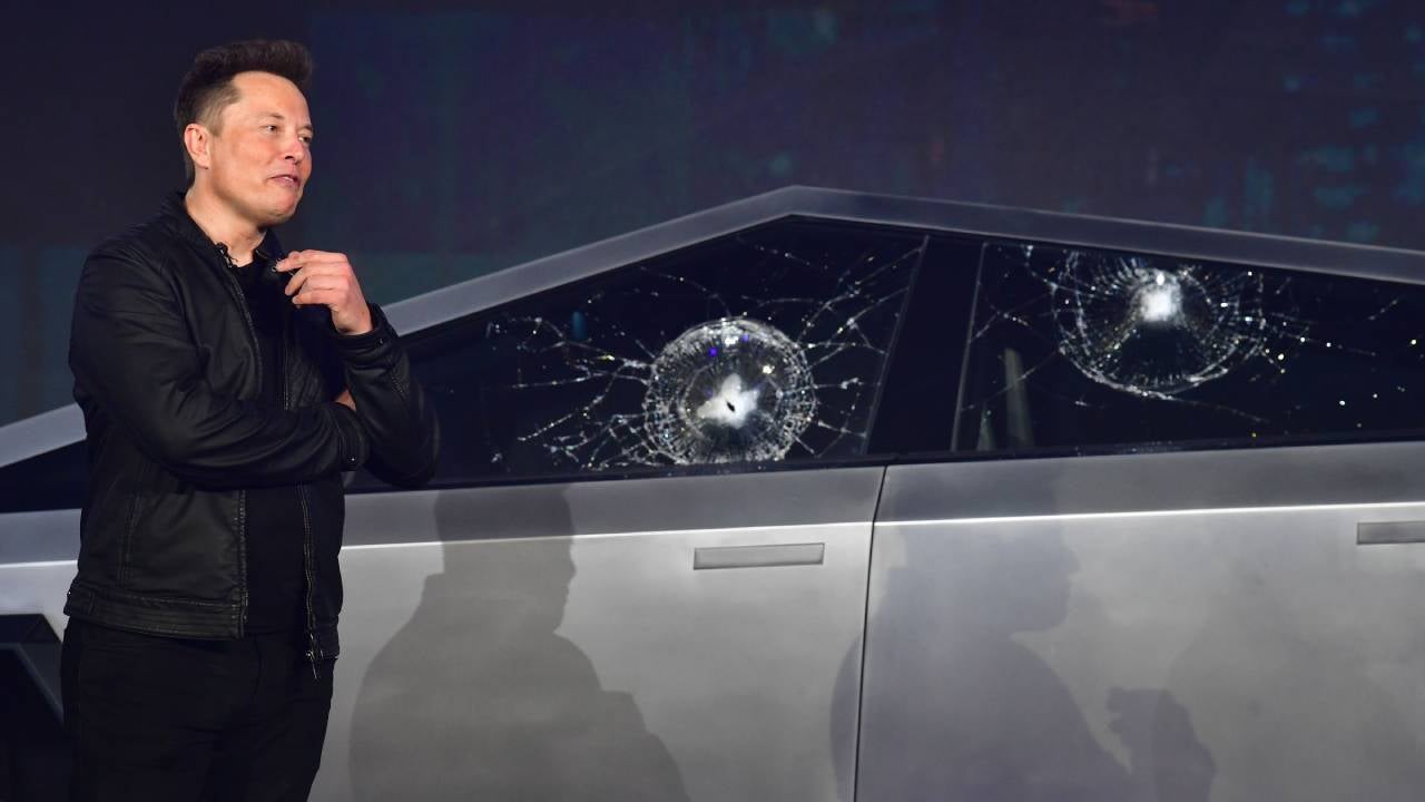 Tesla CEO Elon Musk standing next to a Cybertruck with damaged side windows.