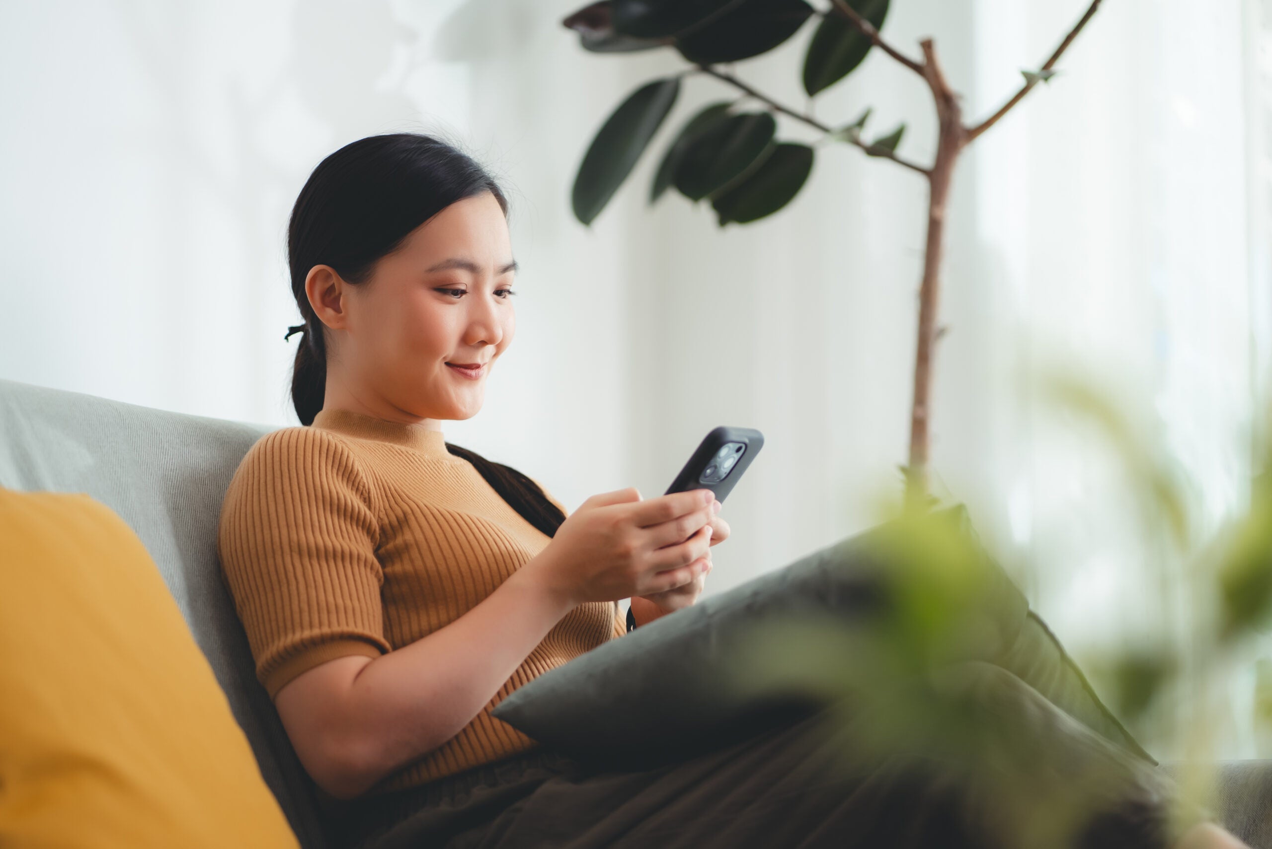 Young woman looks at phone while sitting on a sofa.