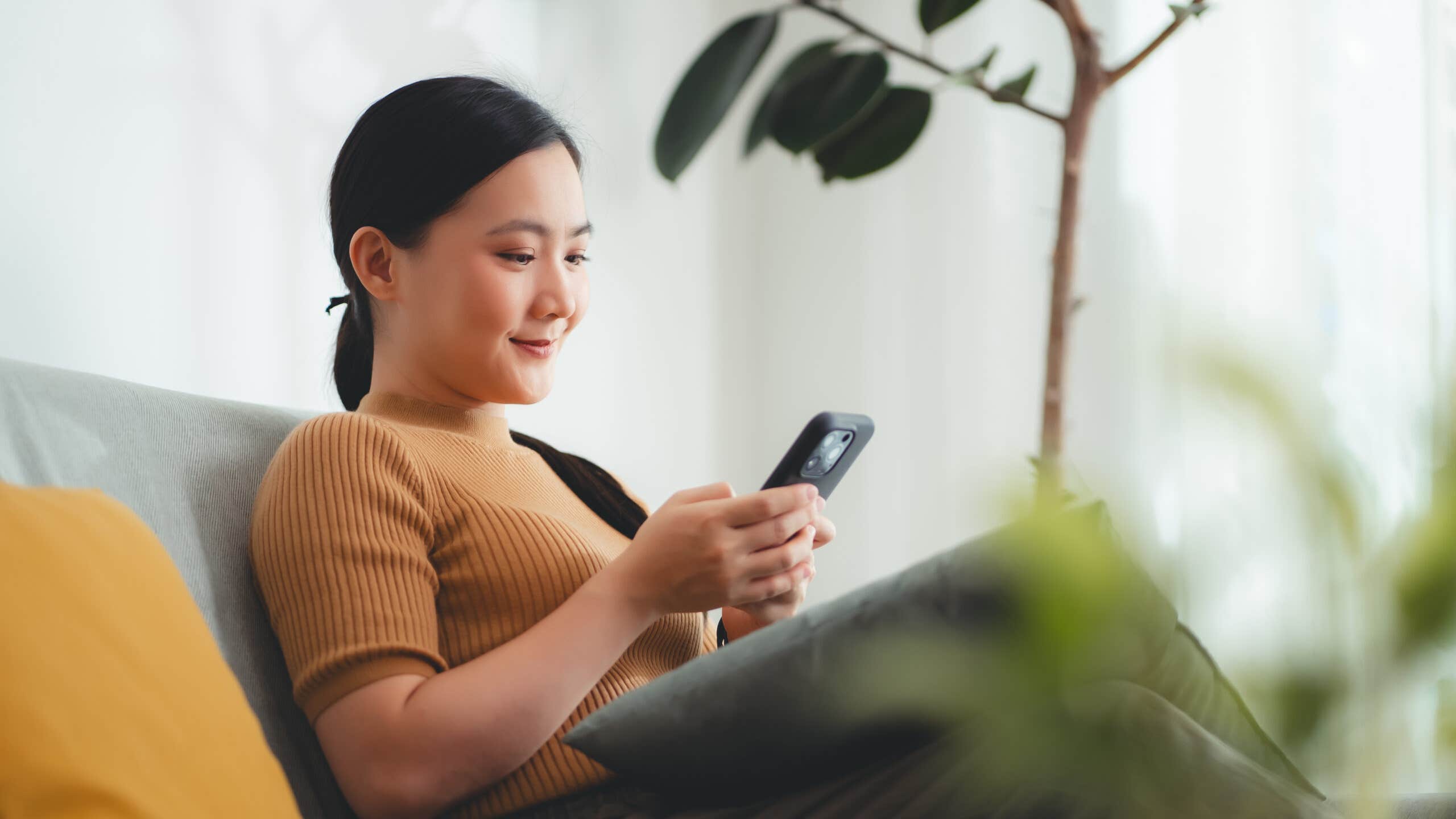 Young woman looks at phone while sitting on a sofa.