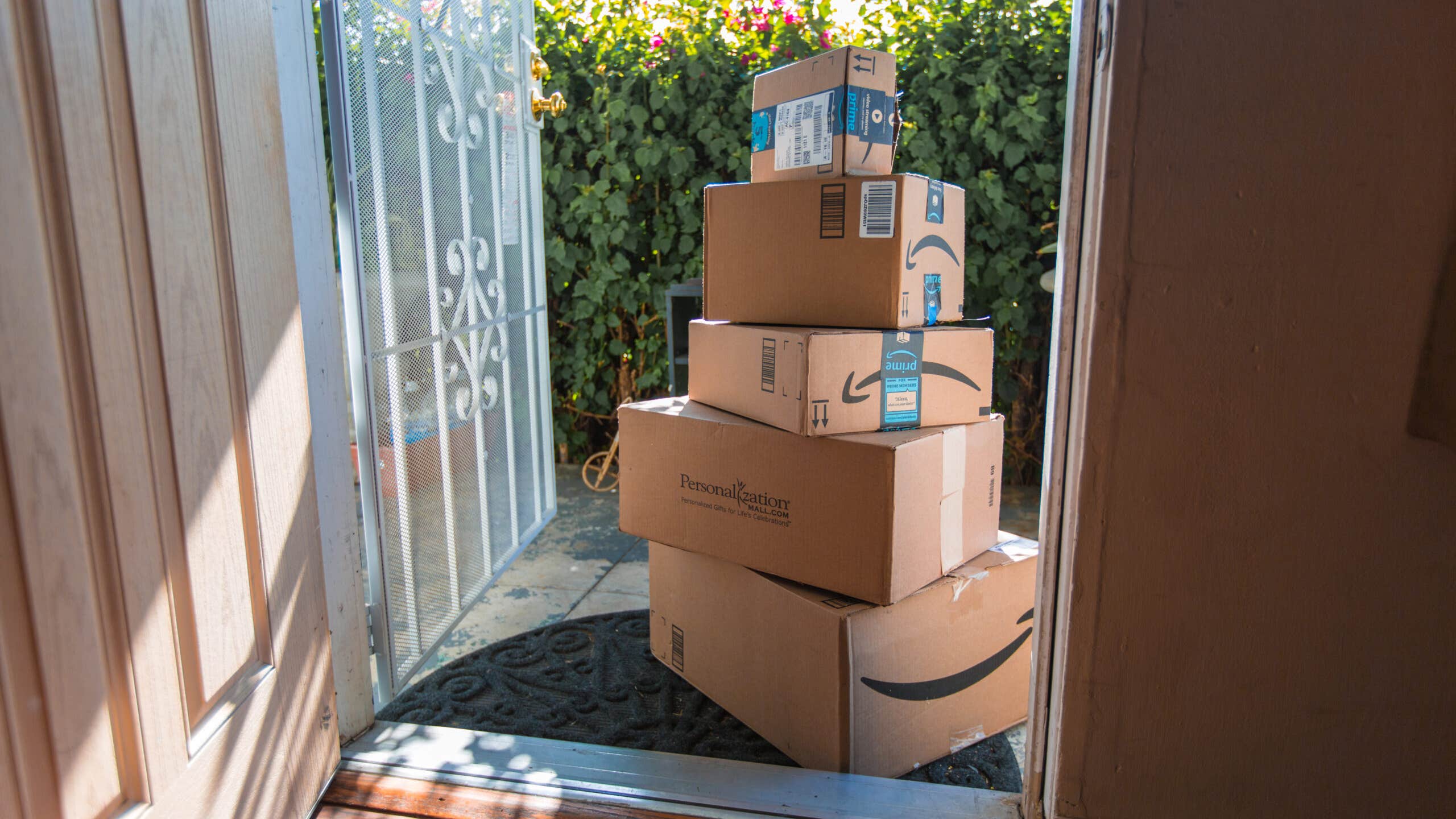Image of Amazon packages stacked up on a sunny front porch.