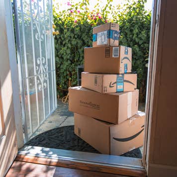 Image of Amazon packages stacked up on a sunny front porch.