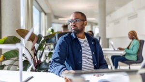Young Black man sits at work looking thoughtful.