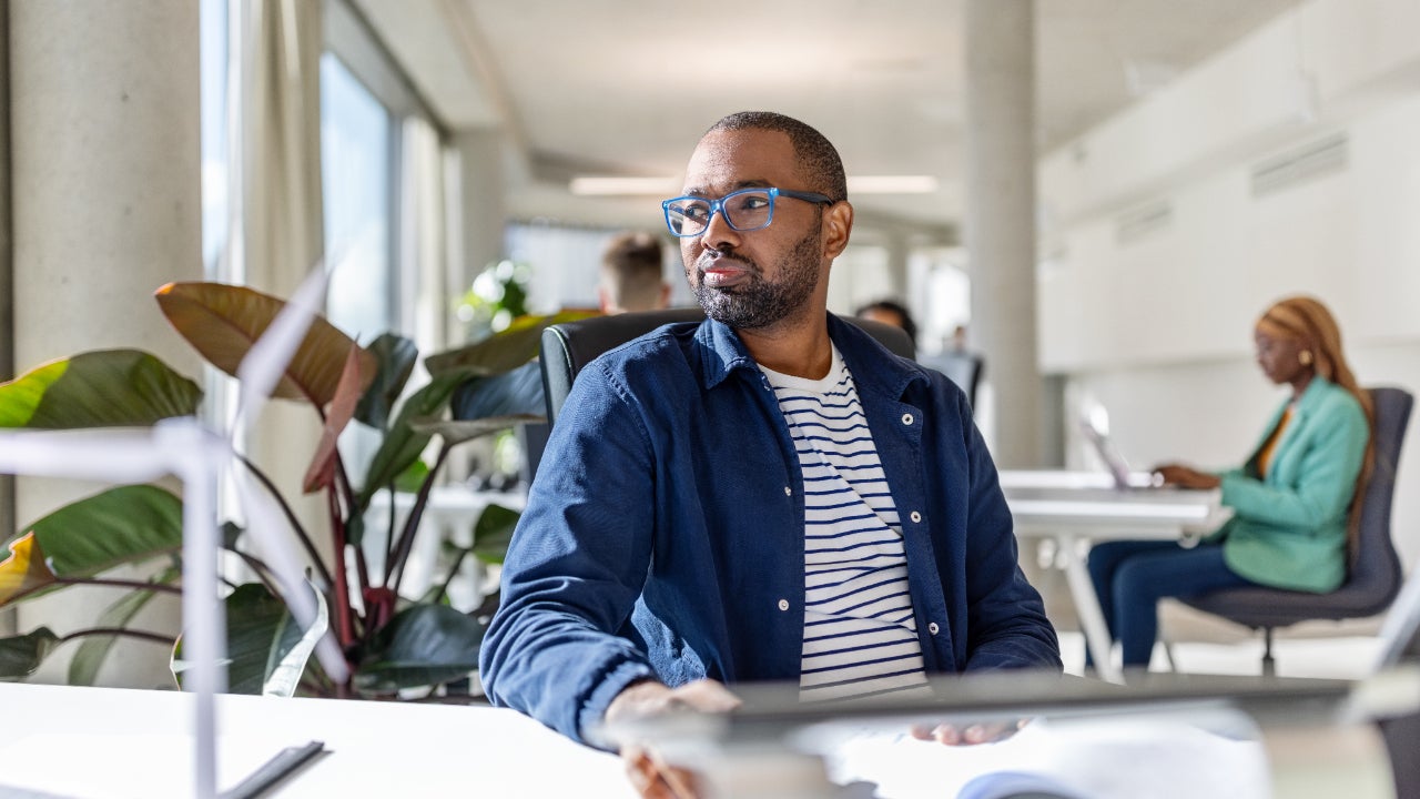 Young Black man sits at work looking thoughtful.
