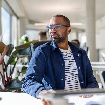 Young Black man sits at work looking thoughtful.