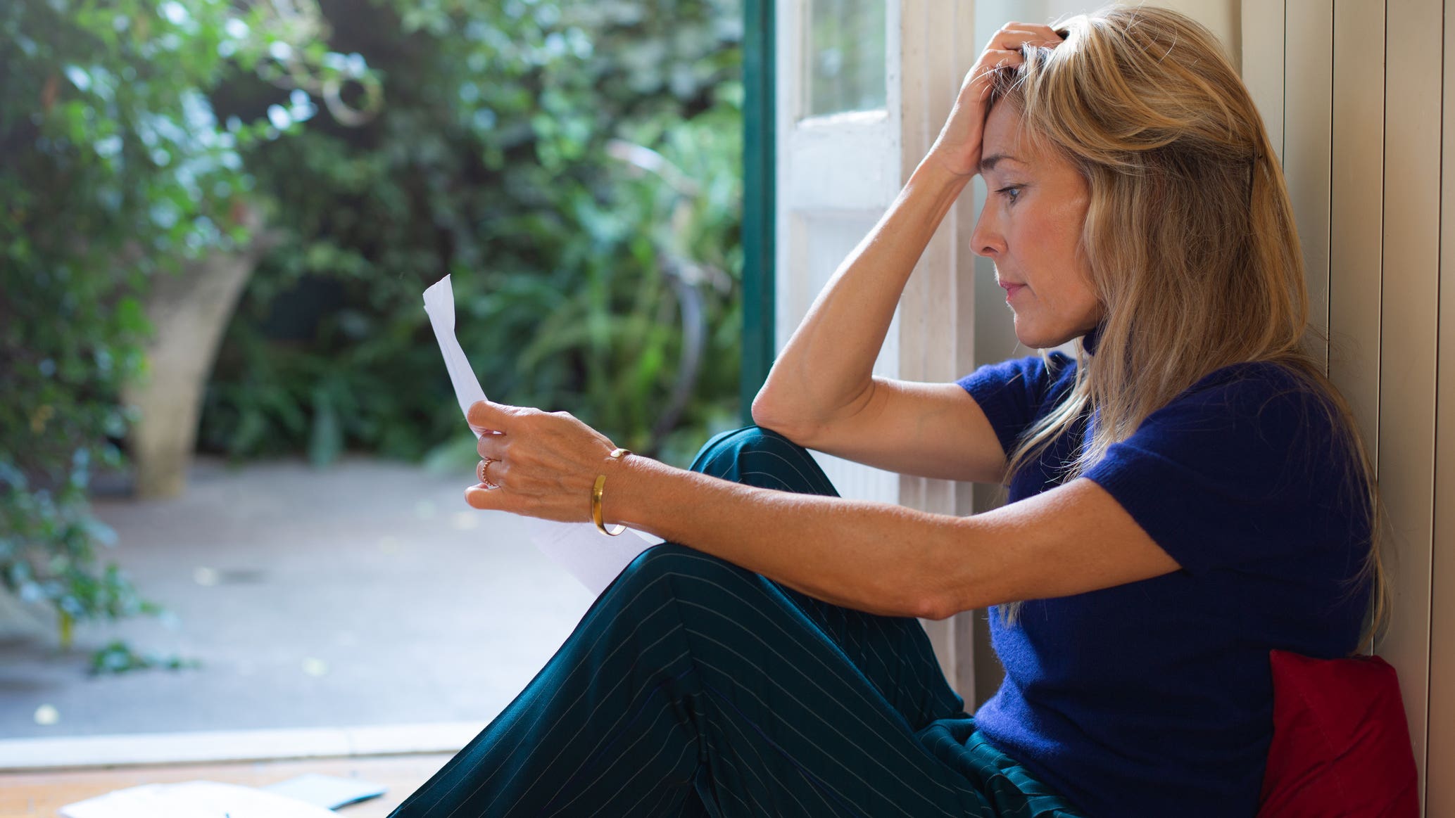 woman with frustrated reaction sitting on floor looking at letter