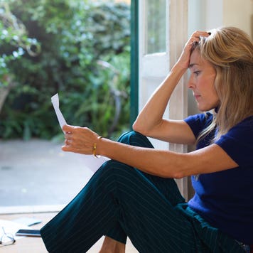woman with frustrated reaction sitting on floor looking at letter
