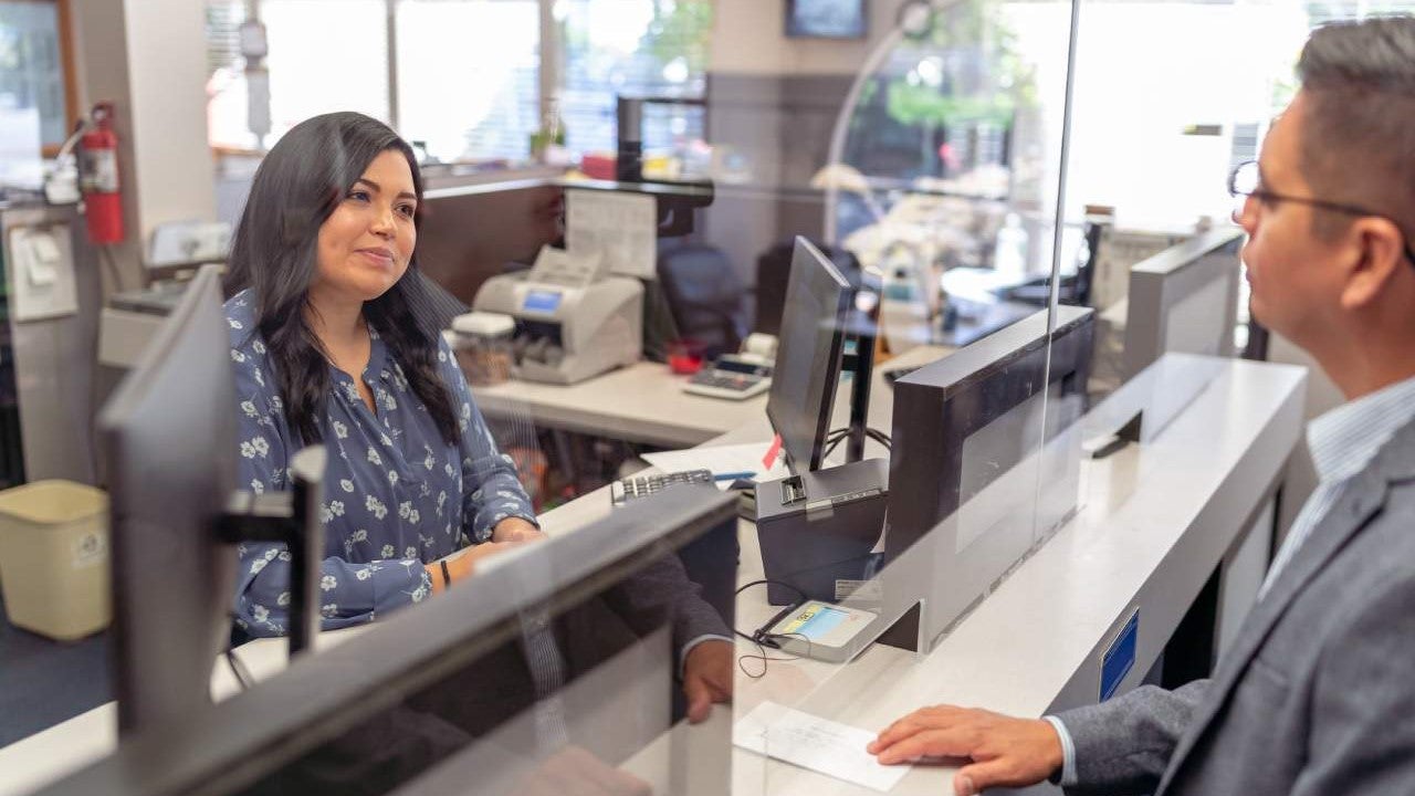 A female bank teller helps a male customer at the bank counter.