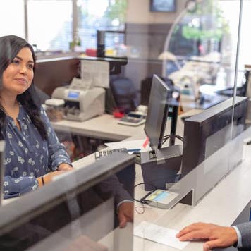 A female bank teller helps a male customer at the bank counter.