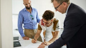 A father and son sign loan documents together while a banker witnesses.