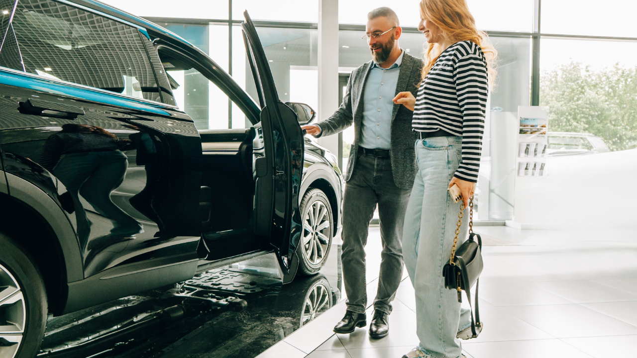 Car salesman showing a new car to a customer in a dealership.