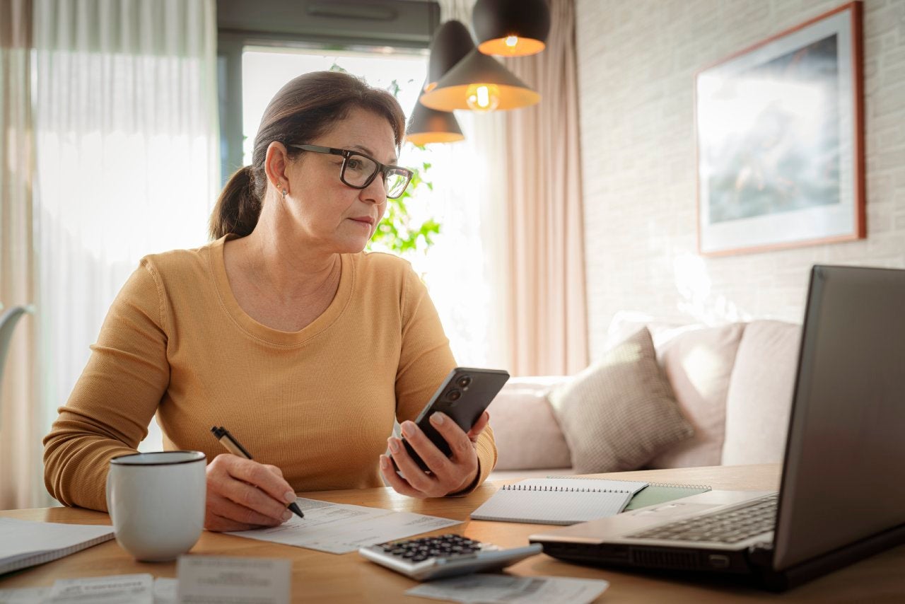 Woman using mobile phone and laptop working from home. Home finances. Calculating budget. Preparing taxes