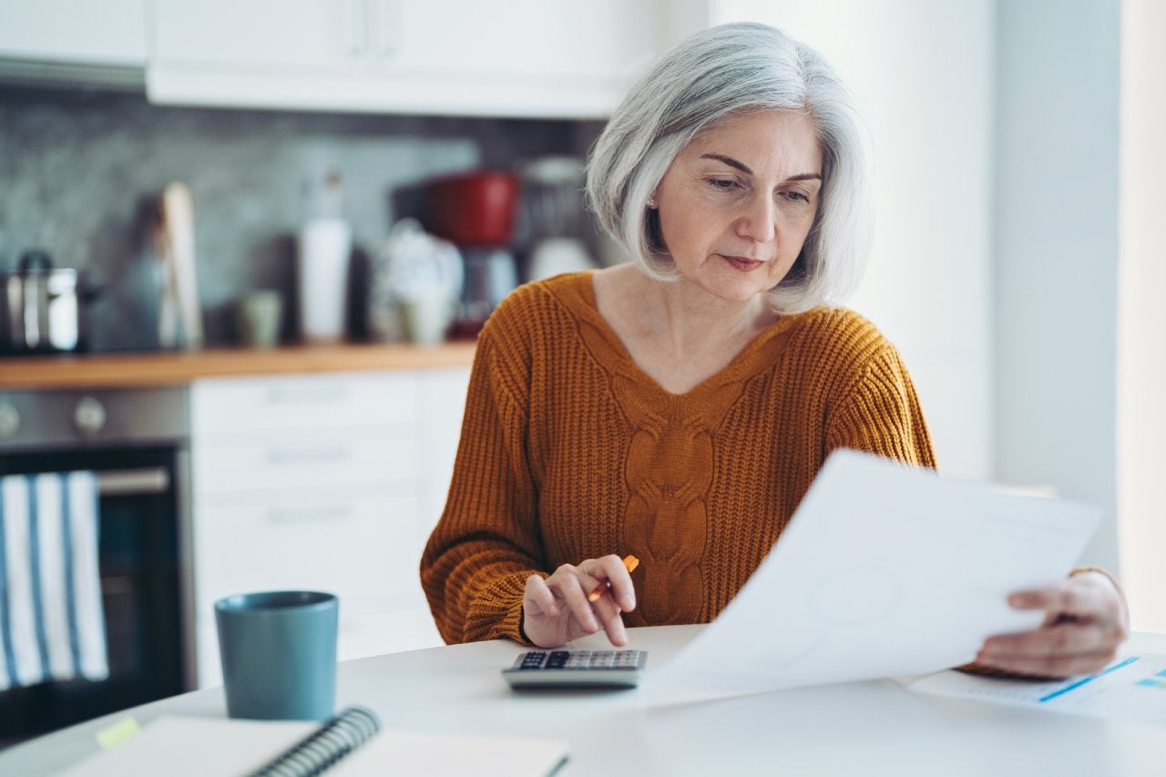 Mature woman with calculator, notebook and documents at home
