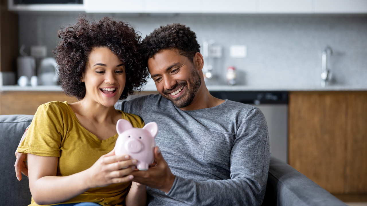 Happy couple at home holding a piggy bank with their savings and smiling - home finances concepts