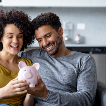 Happy couple at home holding a piggy bank with their savings and smiling - home finances concepts