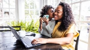 Mother trying to work on laptop while her young daughter is distracting her.