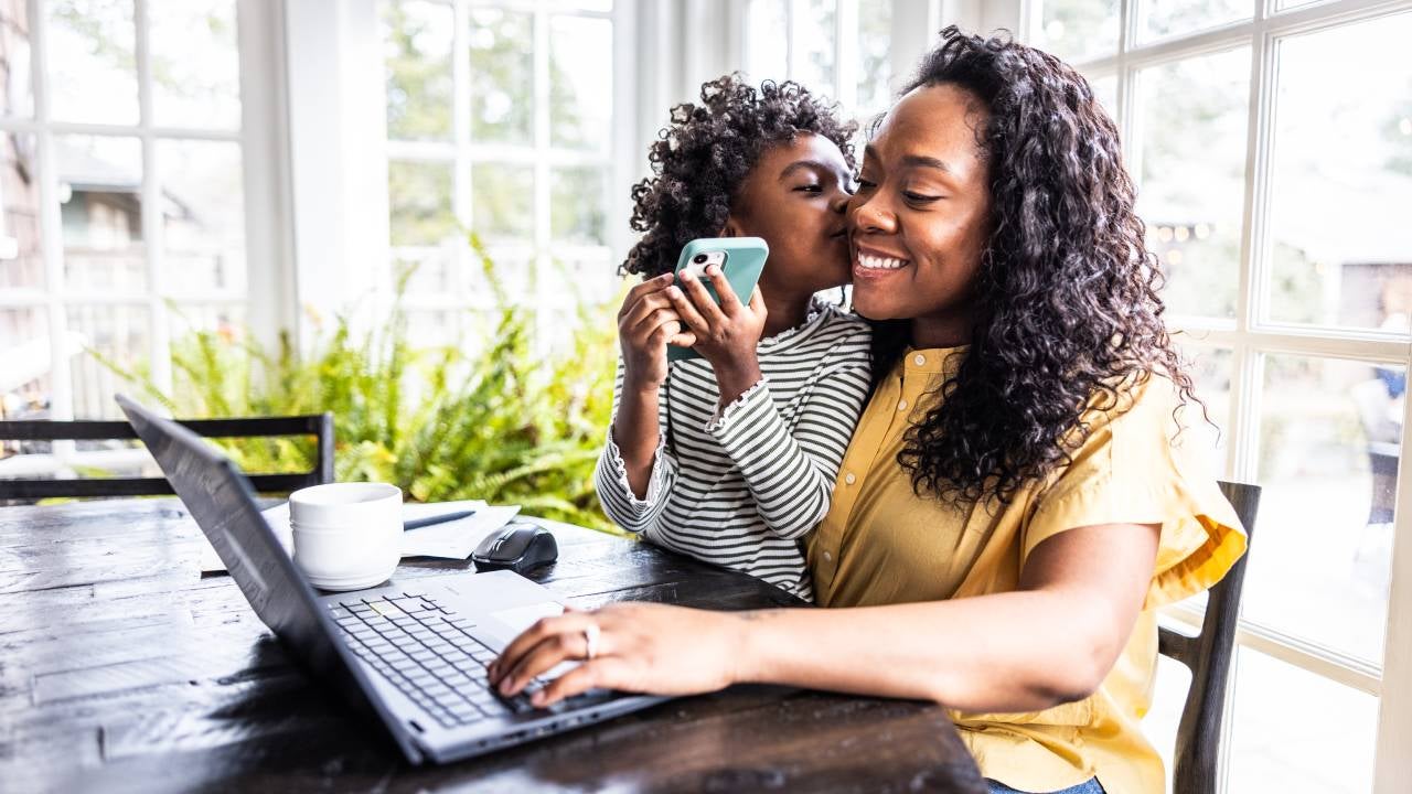 Mother trying to work on laptop while her young daughter is distracting her.