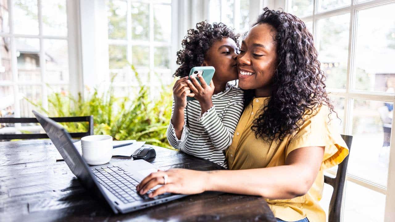 Mother trying to work on laptop while her young daughter is distracting her.