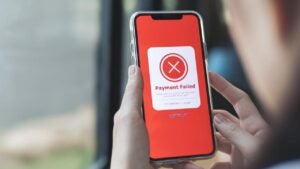 A smartphone being held in a person's had displays the words "Payment Failed" surrounded with a red background with an 'X' above.