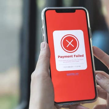 A smartphone being held in a person's had displays the words "Payment Failed" surrounded with a red background with an 'X' above.