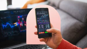 A hand holds an iPhone showing stock charts on the screen.