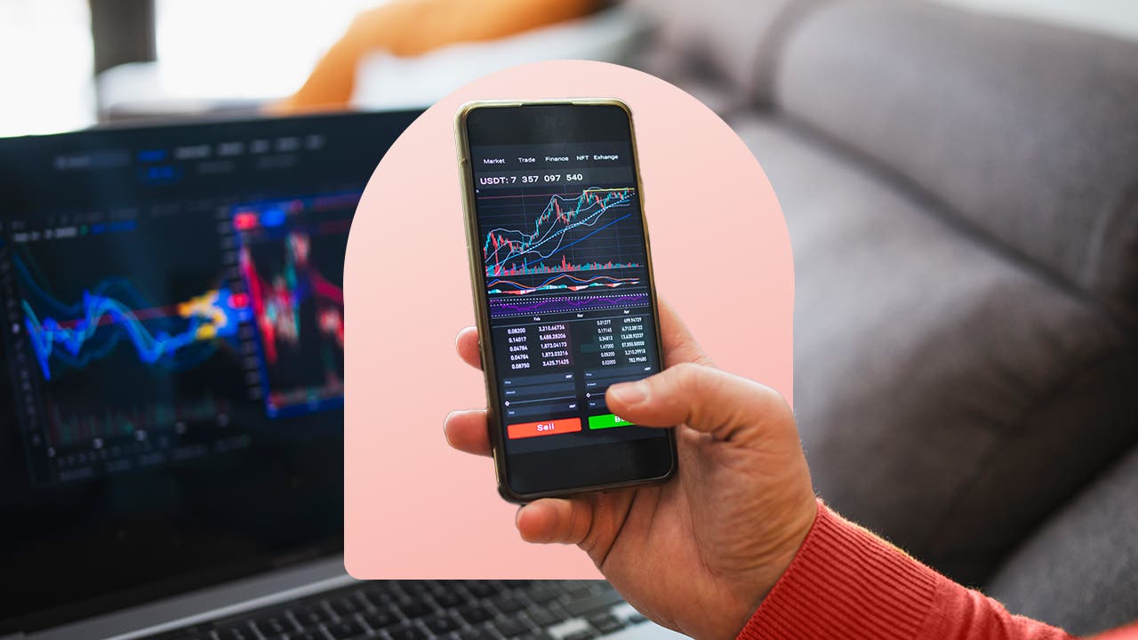 A hand holds an iPhone showing stock charts on the screen.