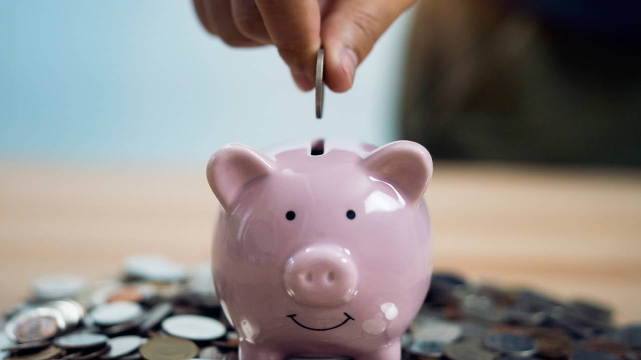 a person putting a coin into a piggy bank, which is on top of coins