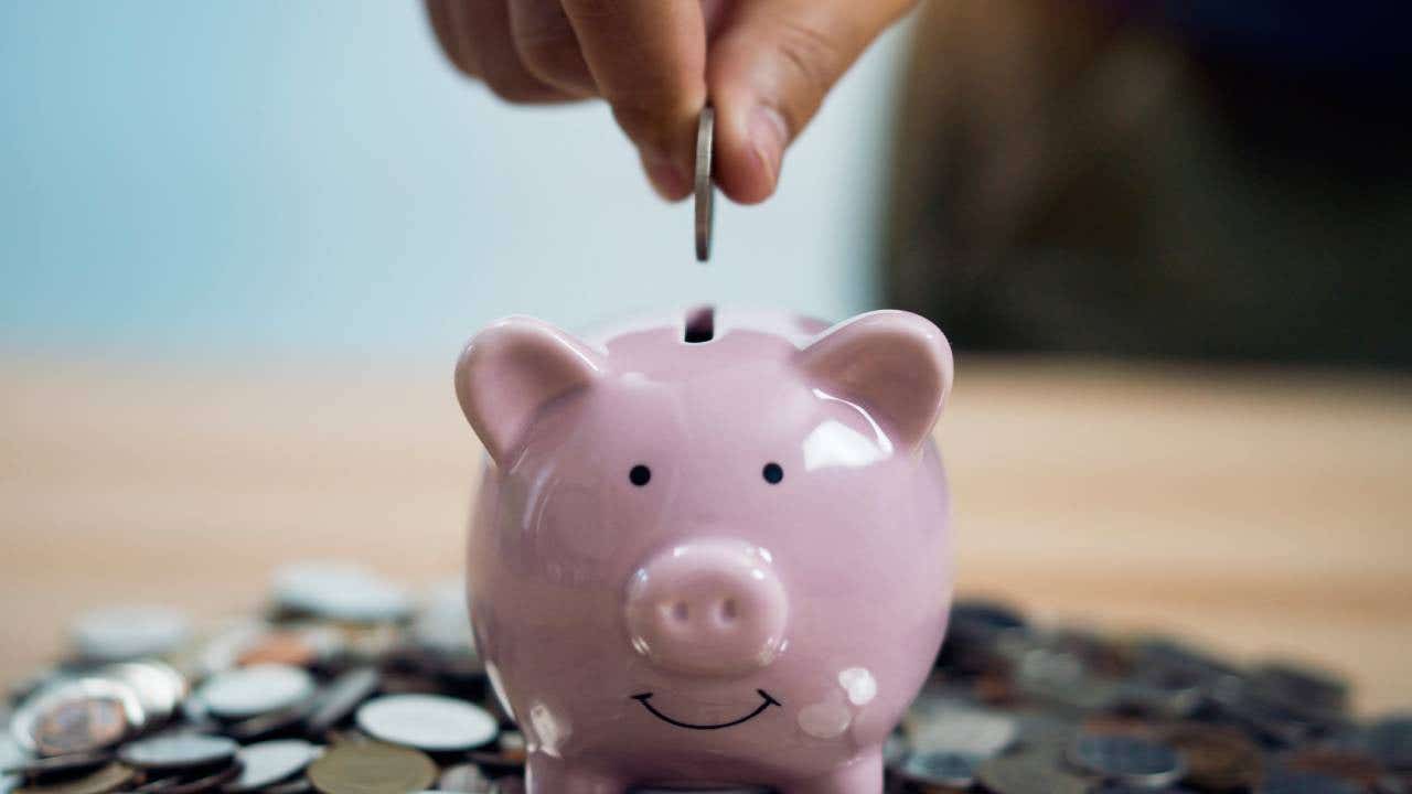 a person putting a coin into a piggy bank, which is on top of coins