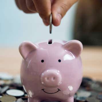 a person putting a coin into a piggy bank, which is on top of coins