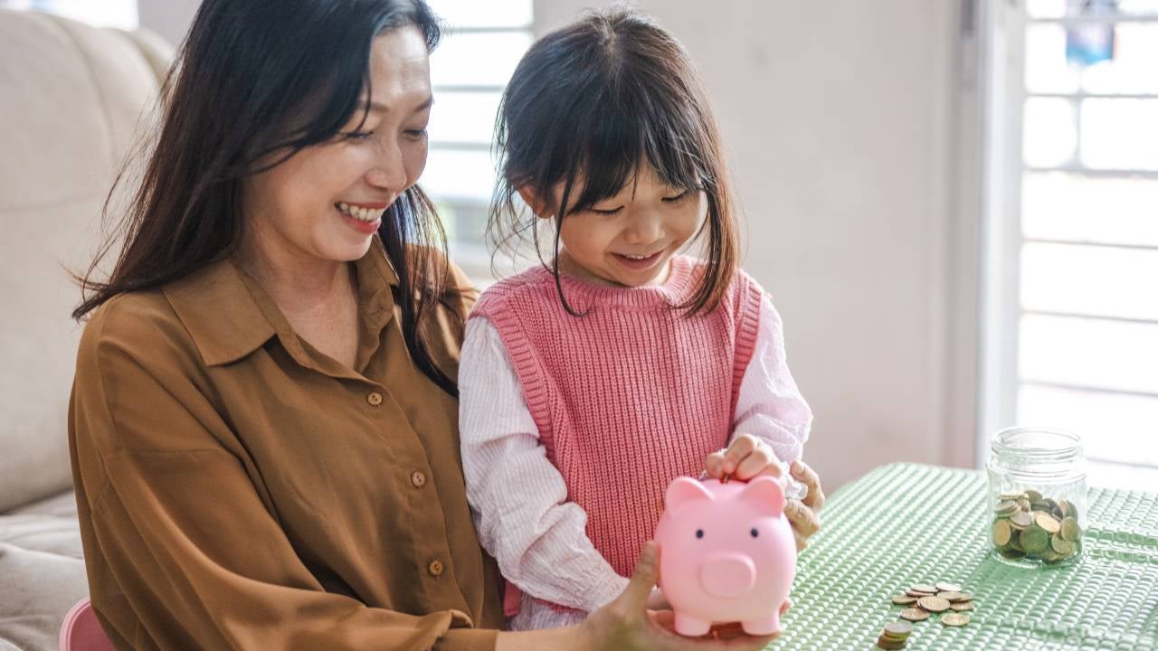 A mom teaches her young daughter about investing with a piggy bank.