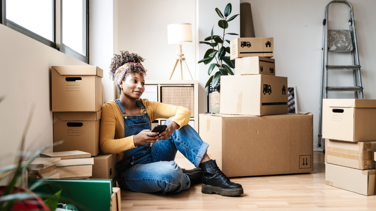 Woman with a cell phone, surrounded by moving boxes.