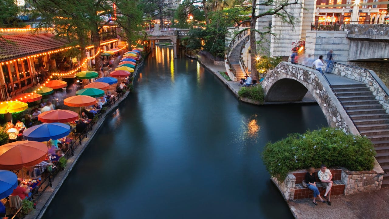 A couple sit along the San Antonio, Texas, river walk at sunset.