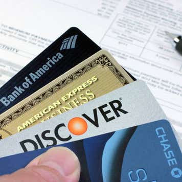 Four real credit and debit cards with a credit cards statement on a desk in the background.