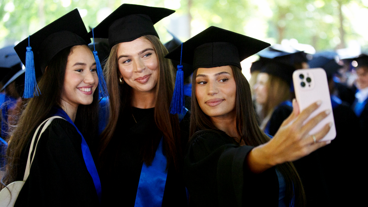 Three female college graduates take a selfie in caps and gowns