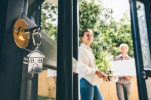 Keys in a door lock with couple celebrating moving day in the background