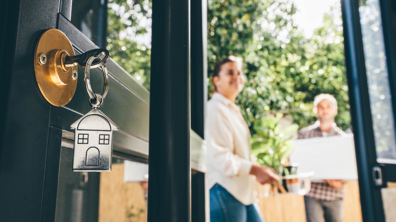 Keys in a door lock with couple celebrating moving day in the background