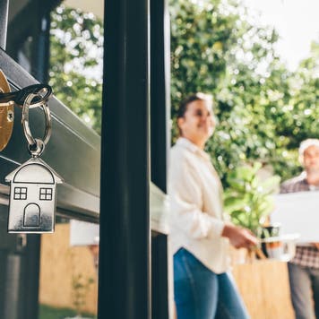 Keys in a door lock with couple celebrating moving day in the background
