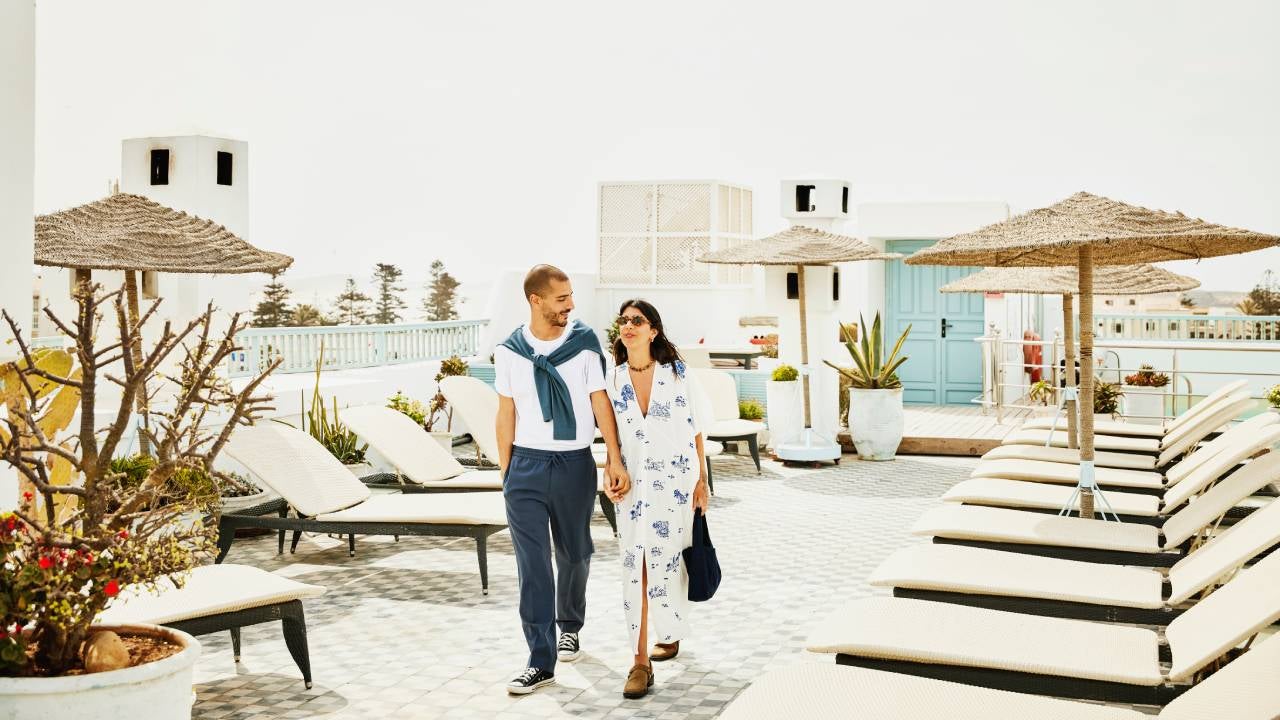 Wide shot couple walking on rooftop deck of luxury tropical resort