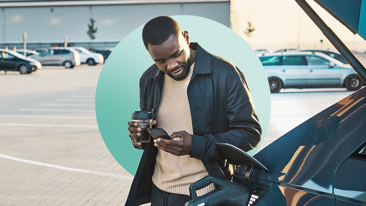 man standing next to car at charging station, looking at cell phone
