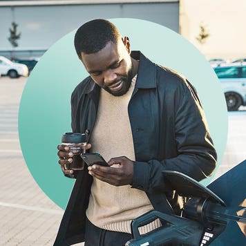 man standing next to car at charging station, looking at cell phone